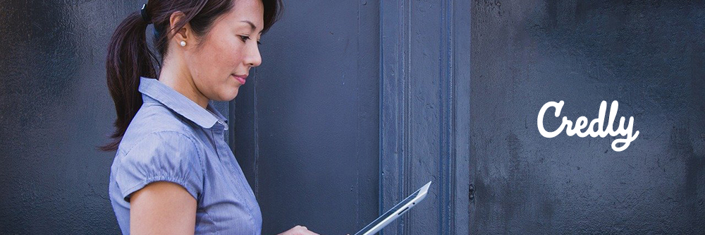Photo of a woman standing holding a laptop with the Credly logo on the right